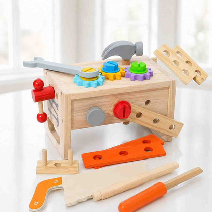 A colorful wooden toy workbench set for children displayed on a bright white surface. The main natural-wood tool bench features colorful interlocking plastic gears, a toy hammer, a wrench, and a built-in vise. Loose wooden toy tools, including a hand saw, a screwdriver, pegs, and building planks in orange and natural wood, are scattered in the foreground.