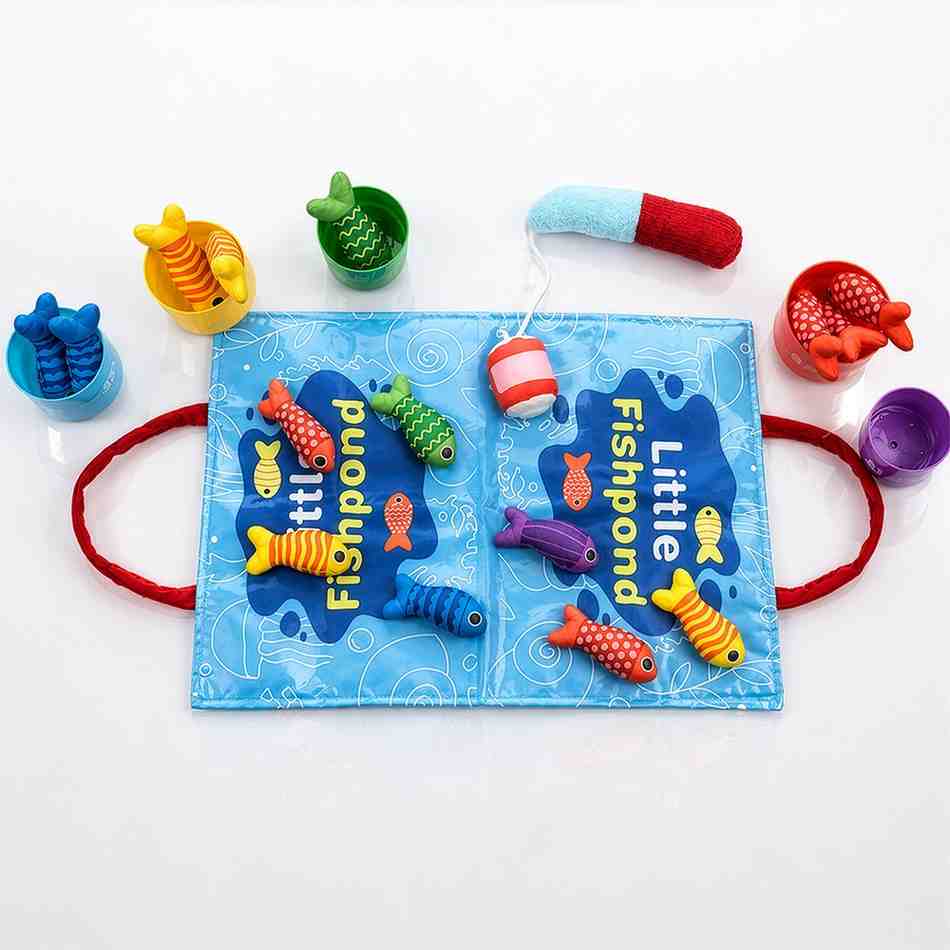 "A professional studio shot of a child's fabric fishing toy set on a white surface. A blue playmat printed with 'Little Fishpond' and underwater graphics sits in the center, featuring red handles on both sides. Colorful plush fish with magnetic elements are scattered across the mat, while a soft fabric fishing rod with a bobber rests nearby. Surrounding the mat are five small, color-coded plastic buckets in blue, yellow, green, red, and purple, used for sorting the matching colored plush fish."